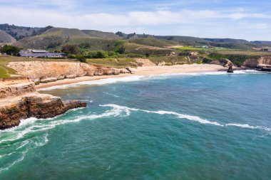 Davenport Sahili 'nin manzaralı manzarası ve Kaliforniya' da 1. karayolu boyunca uzanan kıyı uçurumları, okyanus dalgaları, doğal kaya oluşumları ve arka plandaki tarihi çimento fabrikası.