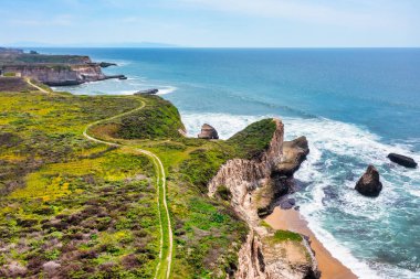 Kaliforniya, Davenport yakınlarındaki dramatik deniz kayalıkları boyunca kıyı şeridi kıvrımları var. Havadan bakıldığında, turkuaz üzerinde doğal bir kaya kemeri görünüyor. Pasifik kıyısındaki ikonik otoyol boyunca dalgalar var..