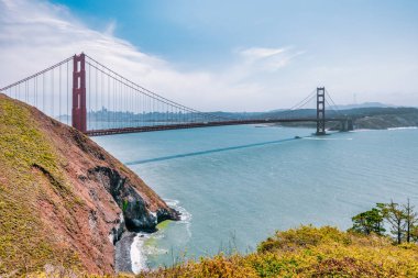 San Francisco Körfezi 'nin mavi suları boyunca uzanan Golden Gate Köprüsü' nün ikonik manzarası Kirby Koyu yakınlarındaki yeşil bir kayalıktan görüldü. Kaliforniya seyahatinin ve doğanın ebedi sembolü.