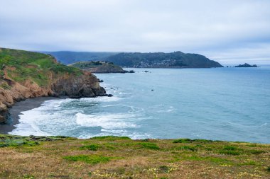 Pasifik, Kaliforniya 'daki Mori Point' ten geniş bir manzara. Çimenli kayalık Pasifik Okyanusu 'na ve bulutlu gökyüzünün altındaki uzak Pacifica İskelesine bakar ve kıyı şeridinin engebeli güzelliğini yakalar.