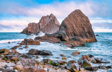 Pasifik, Kaliforniya yakınlarındaki San Pedro Kayası 'nın yakın görüntüsü. Okyanustan yükselen katmanlı volkanik oluşumlar, dramatik bulutlu bir gökyüzünün altında gelgitler ve kayalık kıyılarla çevrili.