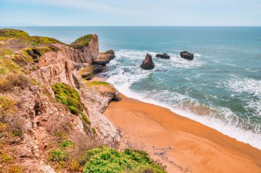 Kaliforniya, Davenport yakınlarındaki sahili ve okyanus dalgalarını. Engebeli kaya oluşumları, Pasifik kıyısı boyunca turkuaz suların üzerinde yükseliyor ve patikadan nefes kesici bir manzara sunuyor.