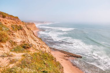 Dalgalar California 'da 1. Otoyol yakınlarındaki engebeli Pasifik Sahili boyunca yontulmuş kumtaşı kayalıklarına ve deniz mağaralarına çarpar. Kayalıkların eteklerinde küçük gizli bir sahil var.