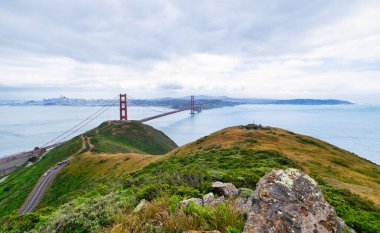 San Francisco Körfezi 'ni kaplayan Golden Gate Köprüsü' nün panoramik manzarası. Şehir manzarası, yemyeşil tepeler ve tekneler bulutlu bir bahar gününde yüksek bir noktadan çekiliyor.