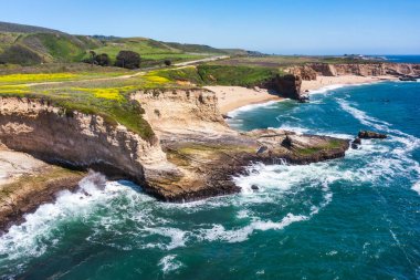 Cotoni-Coast Mandıra Eyalet Plajları 'ndaki Panther Plajı, Kaliforniya. Altın kum, dramatik uçurumlar, turkuaz dalgalar ve 1. Otoyol 'un yanındaki parlak mavi gökyüzünün altındaki manzaralı kıyı şeridi.