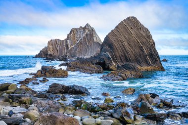 Pasifik, Kaliforniya yakınlarındaki San Pedro Kayası 'nın yakın görüntüsü. Okyanustan yükselen katmanlı volkanik oluşumlar, dramatik bulutlu bir gökyüzünün altında gelgitler ve kayalık kıyılarla çevrili.