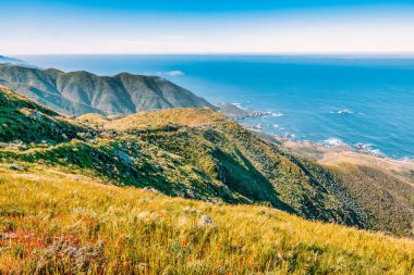 Açık bir ilkbahar gününde, Garrapata Eyalet Parkı 'ndaki Soberanes Kanyonu' nun 1 numaralı otoban boyunca uzanan okyanus ve dağ manzarası taze yeşil tepelerle çevrilidir.