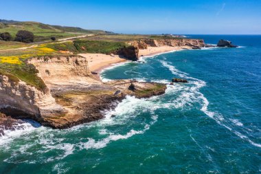 Cotoni-Coast Mandıra Eyalet Plajları 'ndaki Panther Plajı, Kaliforniya. Altın kum, dramatik uçurumlar, turkuaz dalgalar ve 1. Otoyol 'un yanındaki parlak mavi gökyüzünün altındaki manzaralı kıyı şeridi.