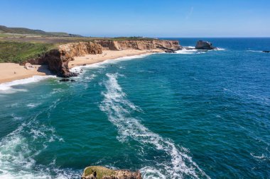 Cotoni-Coast Mandıra Eyalet Plajları 'ndaki Panther Plajı, Kaliforniya. Altın kum, dramatik uçurumlar, turkuaz dalgalar ve 1. Otoyol 'un yanındaki parlak mavi gökyüzünün altındaki manzaralı kıyı şeridi.