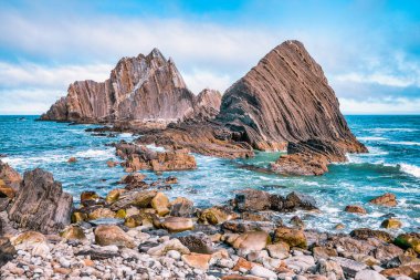 Pasifik, Kaliforniya yakınlarındaki San Pedro Kayası 'nın yakın görüntüsü. Okyanustan yükselen katmanlı volkanik oluşumlar, dramatik bulutlu bir gökyüzünün altında gelgitler ve kayalık kıyılarla çevrili.