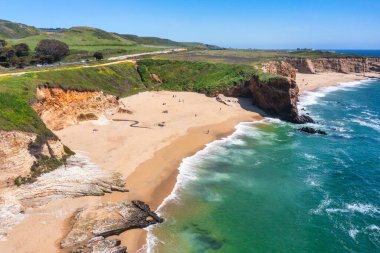 Cotoni-Coast Mandıra Eyalet Plajları 'ndaki Panther Plajı, Kaliforniya. Altın kum, dramatik uçurumlar, turkuaz dalgalar ve 1. Otoyol 'un yanındaki parlak mavi gökyüzünün altındaki manzaralı kıyı şeridi.