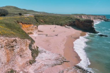 Cotoni-Coast Mandıra Eyalet Plajları 'ndaki Panther Plajı, Kaliforniya. Altın kum, dramatik uçurumlar, turkuaz dalgalar ve 1. Otoyol 'un yanındaki parlak mavi gökyüzünün altındaki manzaralı kıyı şeridi.