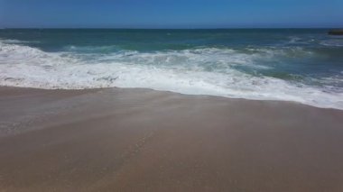 Beyaz deniz köpüklü okyanus dalgaları Kaliforniya, ABD 'de kumlu plajlarda yuvarlanıyor. Sörf, mavi su ve huzurlu yaz atmosferiyle rahatlama sahili arka plan videosu
