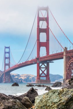 Açık bir günde San Francisco 'daki Golden Gate Köprüsü. İkonik kırmızı asma köprü, Pasifik Okyanusu girişinde ön planda kayalık kıyı şeridi ve uzaklıktaki tepeler boyunca uzanır.