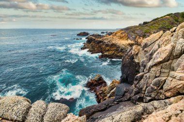 Dramatic Big Sur coastline along Highway 1, California. Waves crash against rugged cliffs, forming turquoise patterns in the Pacific Ocean, showcasing the raw beauty of the California coast