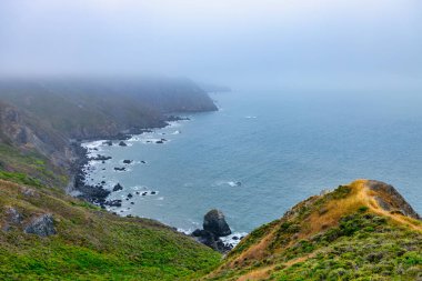 Foggy coastal cliffs at Marin Headlands near San Francisco, California. Rugged shoreline, misty ocean horizon, and green hills along Highway 1 create a dramatic seascape atmosphere