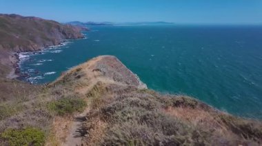 Tennessee Vadisi, Marin Burnu, Kaliforniya, ABD 'de Pasifik Okyanusu' na bakan uçurum kenarındaki yürüyüş yolu videosu. Engebeli kıyı şeridi, dalgalar ve yaz gökyüzü olan manzaralı kıyı manzarası