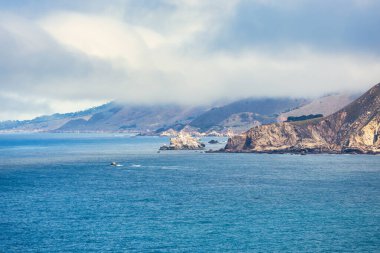 Rocky Big Sur coastline near Point Sur Lighthouse, California, USA. Scenic view of rugged cliffs, Pacific Ocean waves, and coastal fog drifting over the mountains along Highway 1