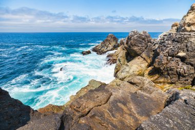 Dramatic Big Sur coastline along Highway 1, California. Waves crash against rugged cliffs, forming turquoise patterns in the Pacific Ocean, showcasing the raw beauty of the California coast