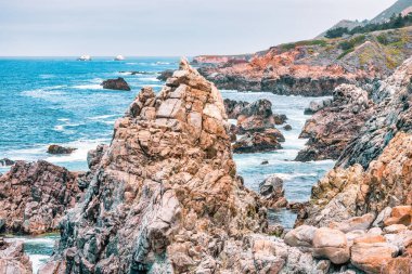 Dramatic Big Sur coastline along Highway 1, California. Waves crash against rugged cliffs, forming turquoise patterns in the Pacific Ocean, showcasing the raw beauty of the California coast