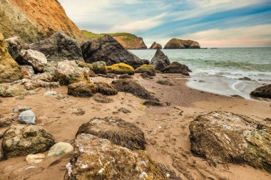 Scenic sunset view at Rodeo Beach in Marin Headlands, California. Dramatic sea stacks and ocean waves glowing in warm evening light, creating a peaceful coastal landscape along Highway 1