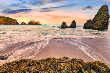 Scenic sunset view at Rodeo Beach in Marin Headlands, California. Dramatic sea stacks and ocean waves glowing in warm evening light, creating a peaceful coastal landscape along Highway 1