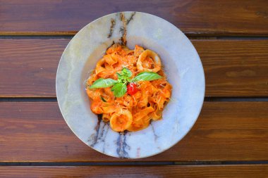 Ahşap arka planda fesleğen yapraklarıyla süslenmiş, kremalı domates soslu, deniz ürünleri ve parmesan peynirli ev yapımı fettucine makarna. Seçici odak, boşluğu kopyala.