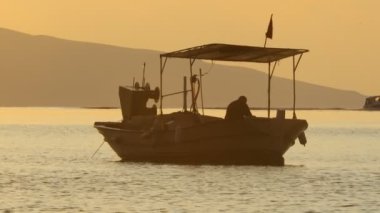 Gün batımında, balıkçı teknesinin zincirini denizden çıkarır. siluet resim.