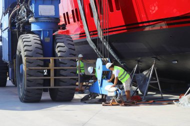 Didim, Aydin, Turkey. 20 June 2022: The huge wheel of the crane carrying the Mega yacht being maintained on land and the technician workers working next to it. 