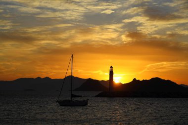 Gün ışığında deniz manzarası. Deniz feneri ve sahilde yelkenliler. Deniz kenti Turgutreis ve muhteşem güneş ışığı