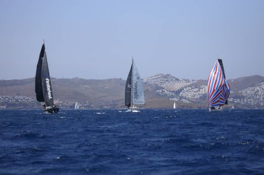 Bodrum, Mugla, Türkiye. 7 Mayıs 2023: Denizci takımı hareket halinde yelkenli sürüyor, arka planda su sıçramaları, dağlar ve deniz manzarası olan yelkenli.. 