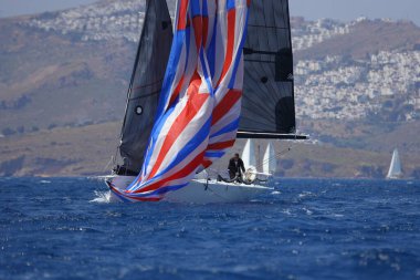 Bodrum, Mugla, Türkiye. 7 Mayıs 2023: Denizci takımı hareket halinde yelkenli sürüyor, arka planda su sıçramaları, dağlar ve deniz manzarası olan yelkenli.. 