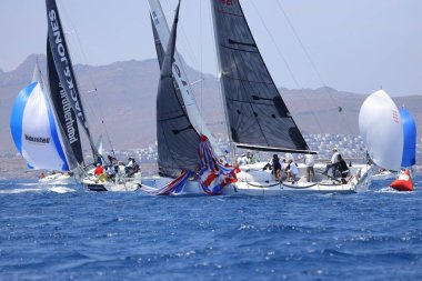 Bodrum, Mugla, Türkiye. 7 Mayıs 2023: Denizci takımı hareket halinde yelkenli sürüyor, arka planda su sıçramaları, dağlar ve deniz manzarası olan yelkenli.. 