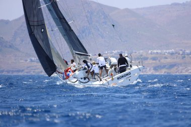 Bodrum, Mugla, Türkiye. 7 Mayıs 2023: Denizci takımı hareket halinde yelkenli sürüyor, arka planda su sıçramaları, dağlar ve deniz manzarası olan yelkenli.. 
