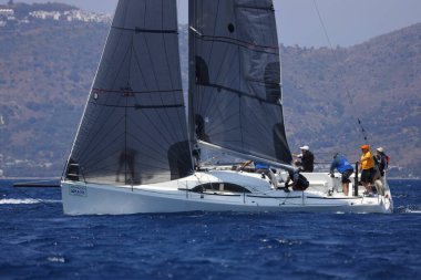Bodrum, Mugla, Türkiye. 7 Mayıs 2023: Denizci takımı hareket halinde yelkenli sürüyor, arka planda su sıçramaları, dağlar ve deniz manzarası olan yelkenli.. 