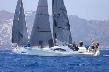 Bodrum, Mugla, Türkiye. 7 Mayıs 2023: Denizci takımı hareket halinde yelkenli sürüyor, arka planda su sıçramaları, dağlar ve deniz manzarası olan yelkenli.. 
