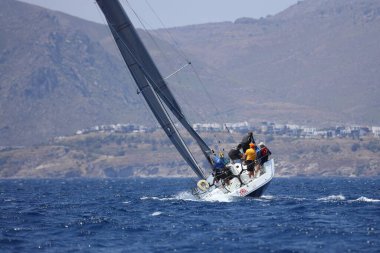 Bodrum, Mugla, Türkiye. 7 Mayıs 2023: Denizci takımı hareket halinde yelkenli sürüyor, arka planda su sıçramaları, dağlar ve deniz manzarası olan yelkenli.. 