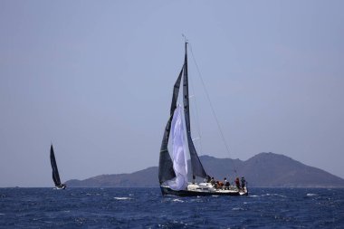 Bodrum, Mugla, Türkiye. 7 Mayıs 2023: Denizci takımı hareket halinde yelkenli sürüyor, arka planda su sıçramaları, dağlar ve deniz manzarası olan yelkenli.. 