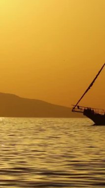Denizde yelkenli. Denizin üzerinde deniz manzaralı altın gün doğumu. Gündoğumunda yat gezintisi. Güzel bir yelkenli ile deniz manzarası. Yelkenliyle turizm turizmi yapıyor. Dikey video.