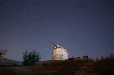 Gece gökyüzündeki yel değirmenini mahveder. Önünde bir dağ tepesi olan Samanyolu 'nun yıldızlarının görüntüsü. Gece gökyüzü doğa yaz manzarası. Perseid Meteor Yağışı gözlemi