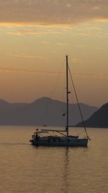 Denizde yelkenli. Denizin üzerinde deniz manzaralı altın gün doğumu. Gündoğumunda yat gezintisi. Güzel bir yelkenli ile deniz manzarası. Yelkenliyle turizm turizmi yapıyor. Dikey video.