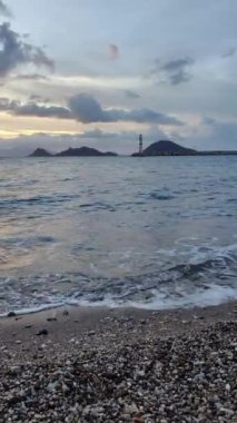 Gün batımında deniz manzarası. Sahildeki deniz feneri. Deniz kenti Turgutreis ve muhteşem gün batımı. Sosyal medya için dikey video.