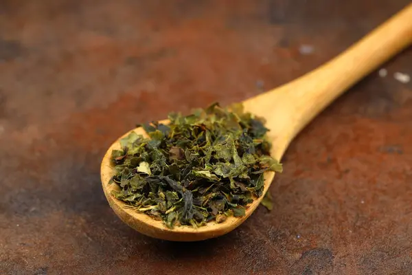 Green tea with herbs in wooden spoons on a wooden board