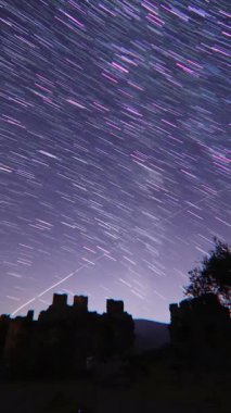 Gecenin eski kalesi. Gece gökyüzünde hareket eden yıldızların zaman çizelgesi. Önünde bir dağ tepesi olan Samanyolu 'nun yıldızlarının görüntüsü. Perseid Meteor yağmuru gözlemi. dikey video.