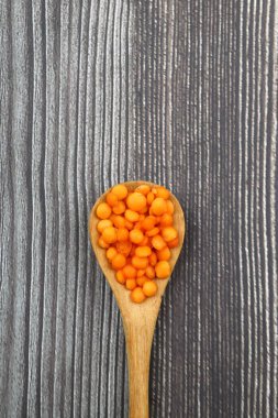 Tahta bir kaşıkta kırmızı mercimek, eski bir tahta masada, yakın plan. Vejetaryen yemeği..