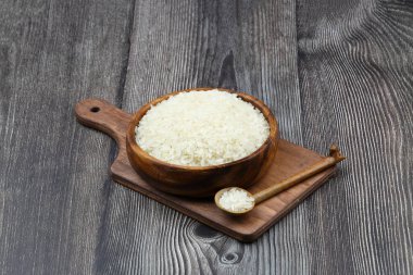 Siyah arka planda çiğ beyaz pirinç. Ahşap tabakta uzun pişmemiş pirinç. Doğal organik gıda. Geleneksel Asya mısır gevreği kültürü.