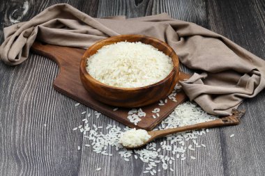 Ahşap arka planda çiğ beyaz pirinç. Ahşap tabakta uzun pişmemiş pirinç. Doğal organik gıda. Geleneksel Asya mısır gevreği kültürü.