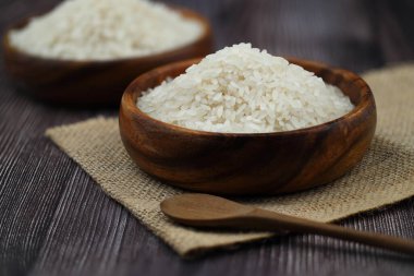 Ahşap arka planda çiğ beyaz pirinç. Ahşap tabakta uzun pişmemiş pirinç. Doğal organik gıda. Geleneksel Asya mısır gevreği kültürü.