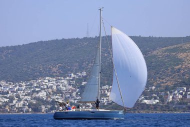 Bodrum, Hindi. 28 Nisan 2024: Yelkenliler Ege Denizi 'nin mavi sularında, ünlü tatil beldesi Bodrum' un kıyılarında rüzgarlı havada yelken açıyorlar..