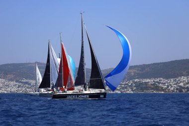 Bodrum, Hindi. 28 Nisan 2024: Yelkenliler Ege Denizi 'nin mavi sularında, ünlü tatil beldesi Bodrum' un kıyılarında rüzgarlı havada yelken açıyorlar..